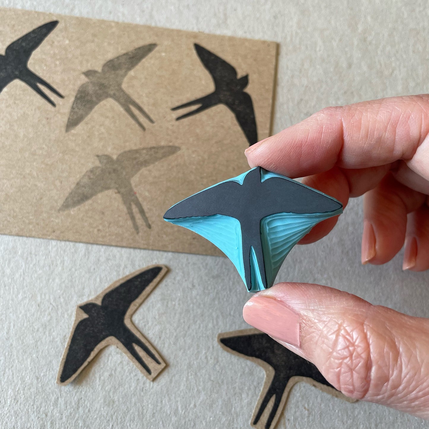 Hand holding a blue rubber carved in the shape of a swallow silhouette bird