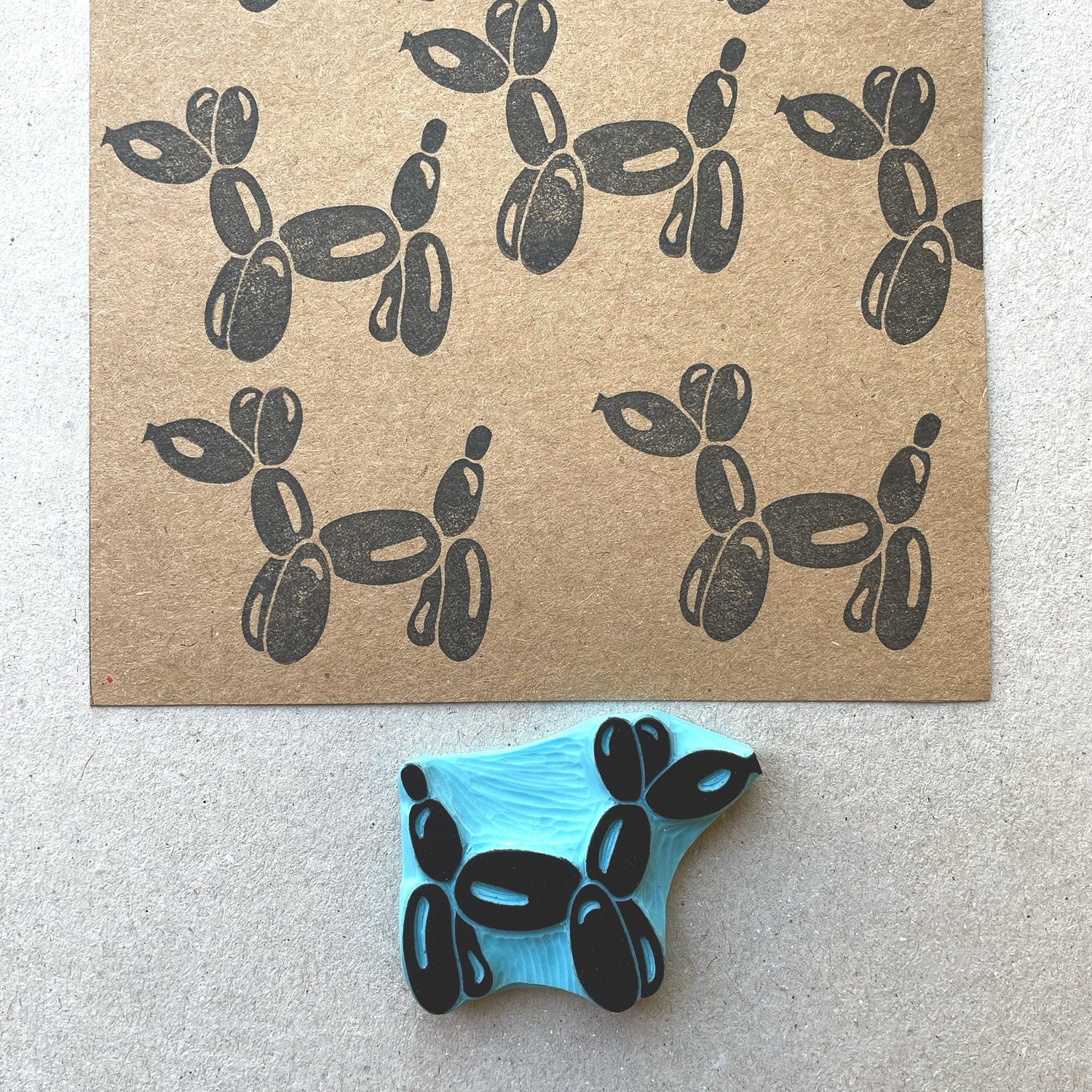 Hand carved rubber stamp of a balloon dog with stamped pattern on brown paper