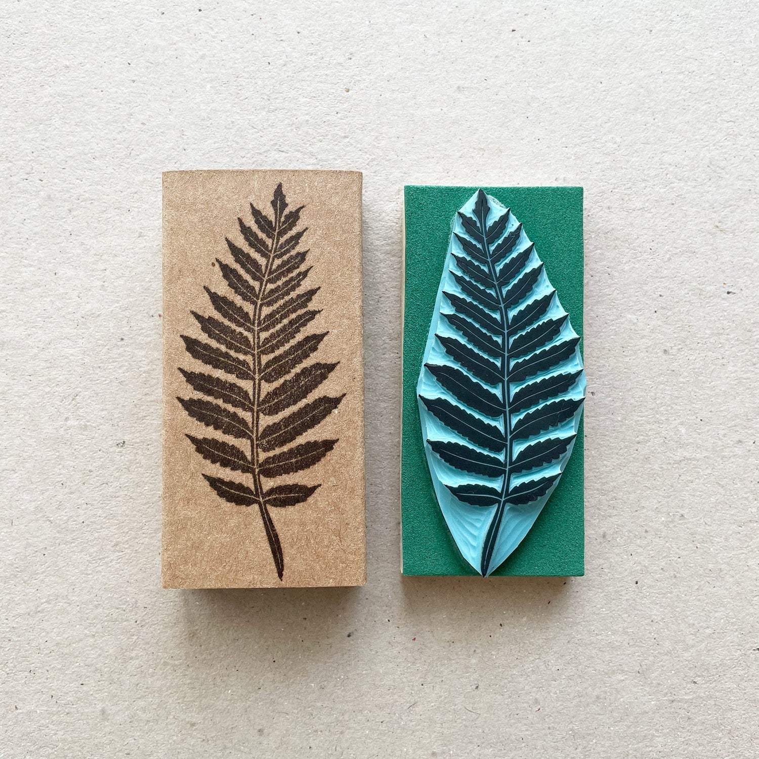 Hand carved rubber stamp with detailed fern leaf design shown beside stamped image on cardboard.