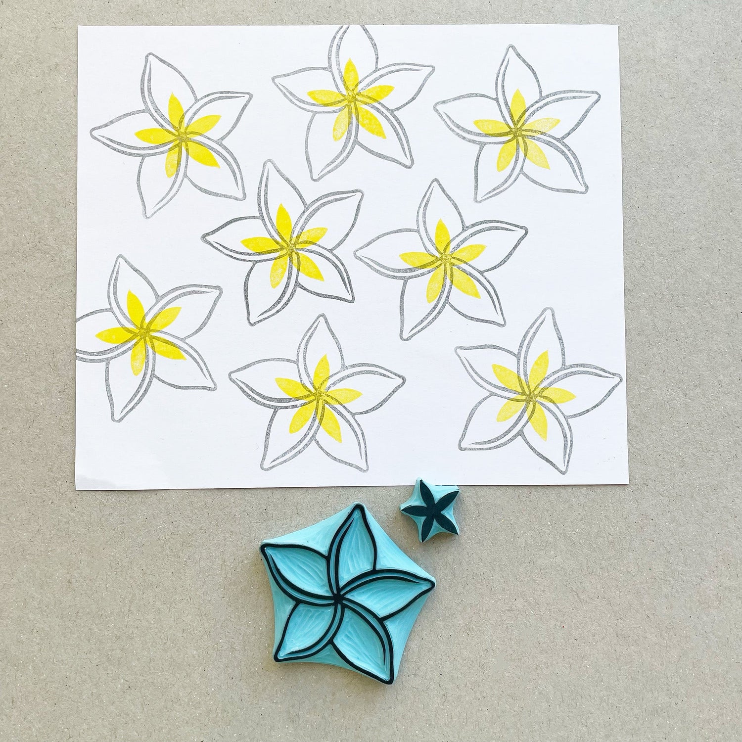 Hand carved rubber stamps of plumeria flowers with yellow and grey ink on white paper