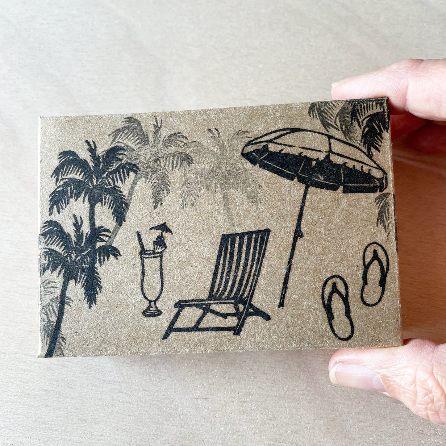hand holding a closed custom cardboard box stamped with beach theme images in black