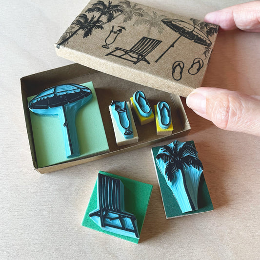 hand closing a cardboard box containing some beach theme rubber stamps inside and some outside the box