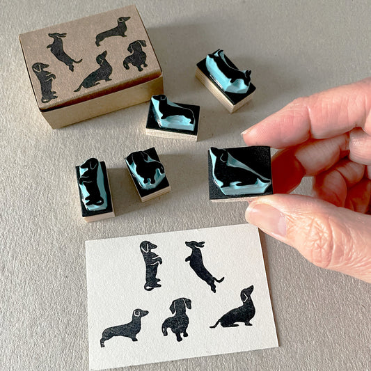 Hand holding a mini dachshund rubber stamp with five sausage dog stamps and printed impressions