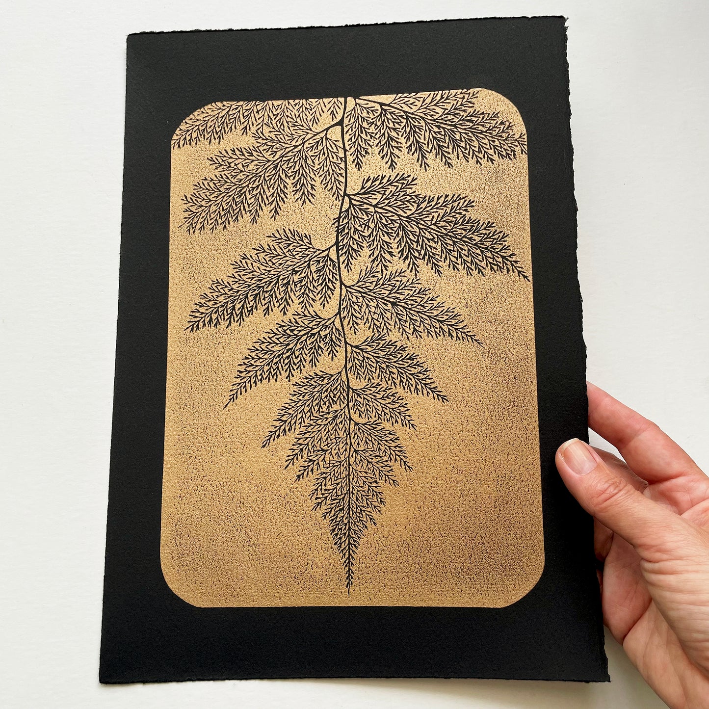 Block print of a fern, gold ink on black paper