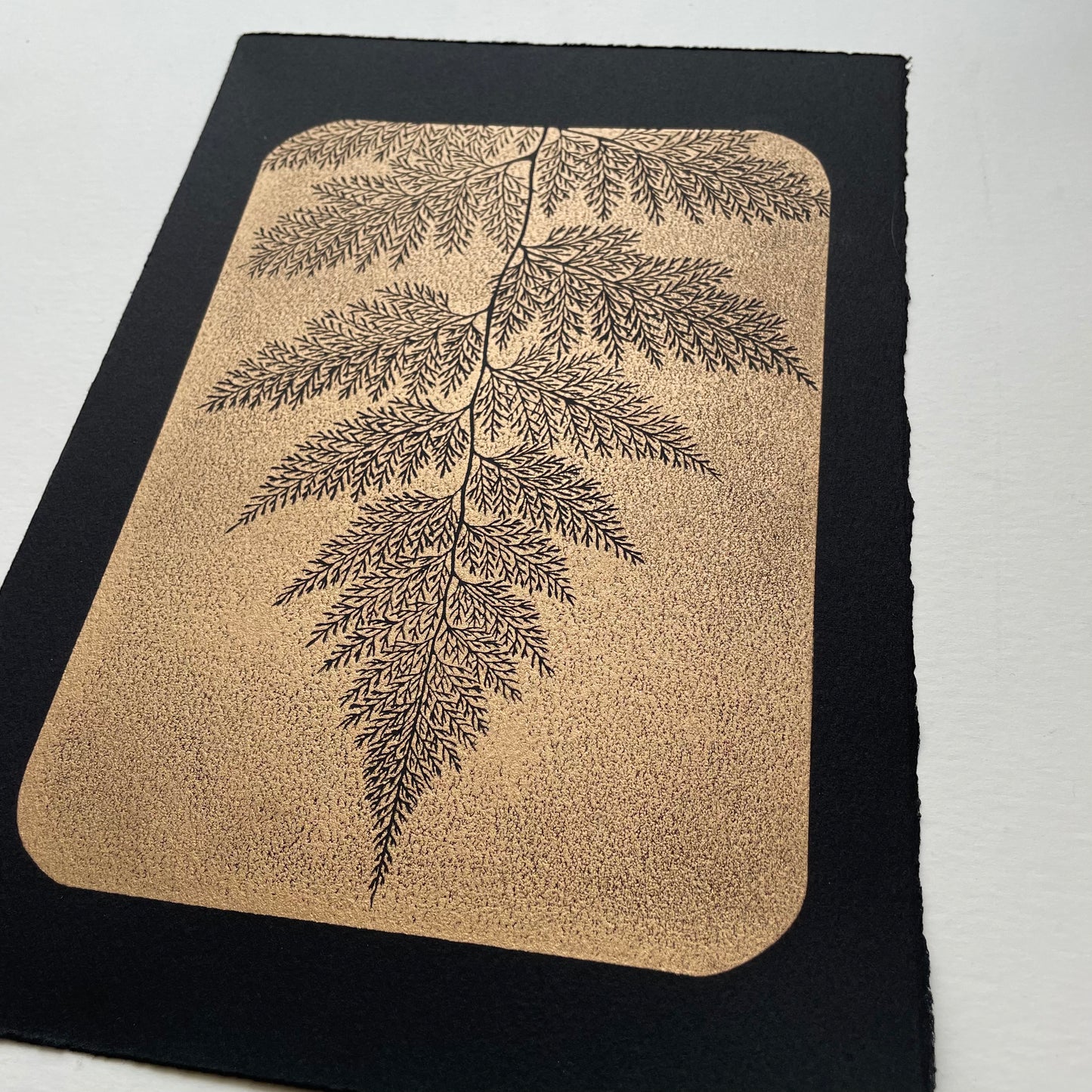 Block print of a fern, gold ink on black paper