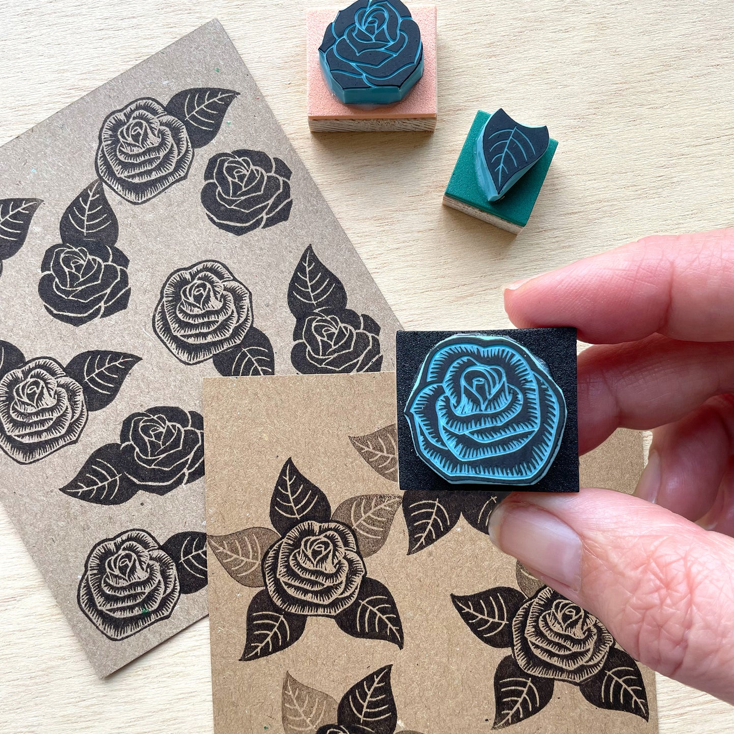 Rose stamp and ink pad on a wooden surface with a hand holding a stamped rose.
