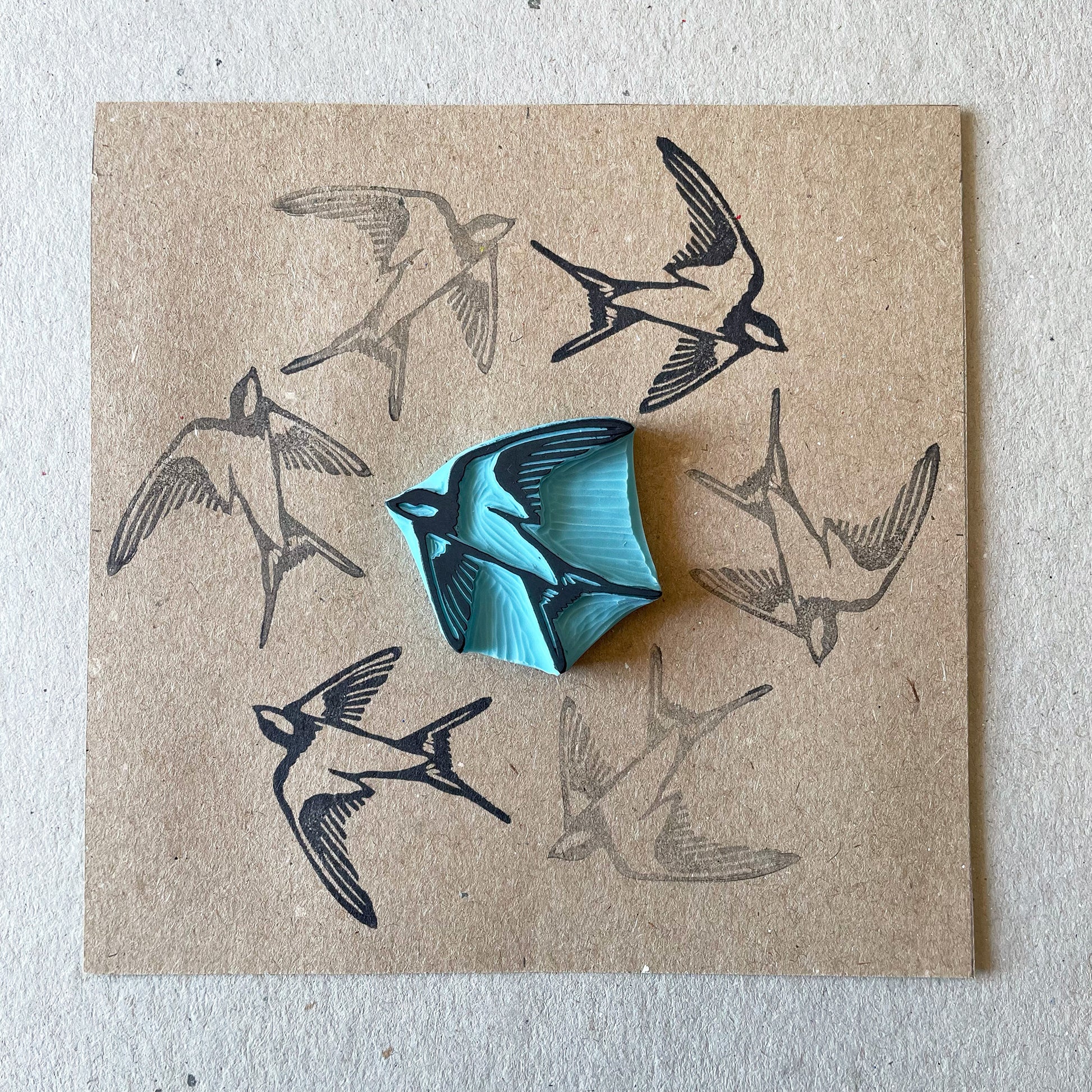 square kraft paper with a swallow bird rubber stamp in the middle of the paper surrounded by the stamped bird in a circle design around the stamp