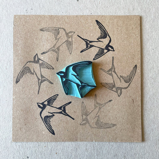 square kraft paper with a swallow bird rubber stamp in the middle of the paper surrounded by the stamped bird in a circle design around the stamp