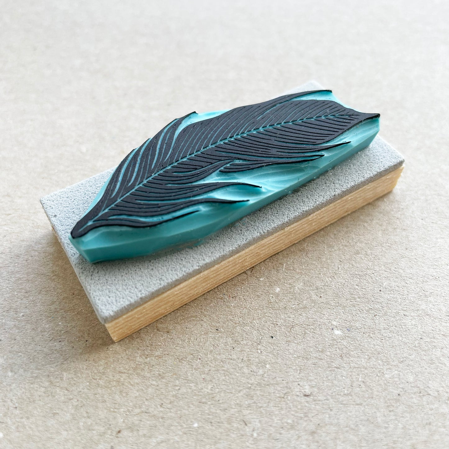 a hand-carved rubber stamp with a feather design, with wood base